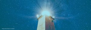 Lighthouse shining at night under a star-filled sky