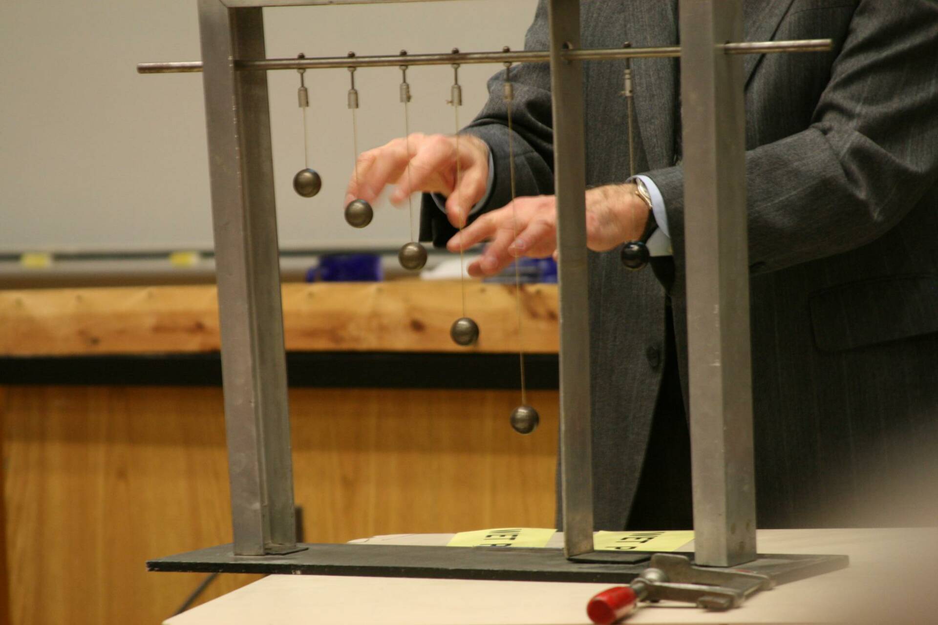 A professor demonstrates a physics experiment using a set of hanging pendulums