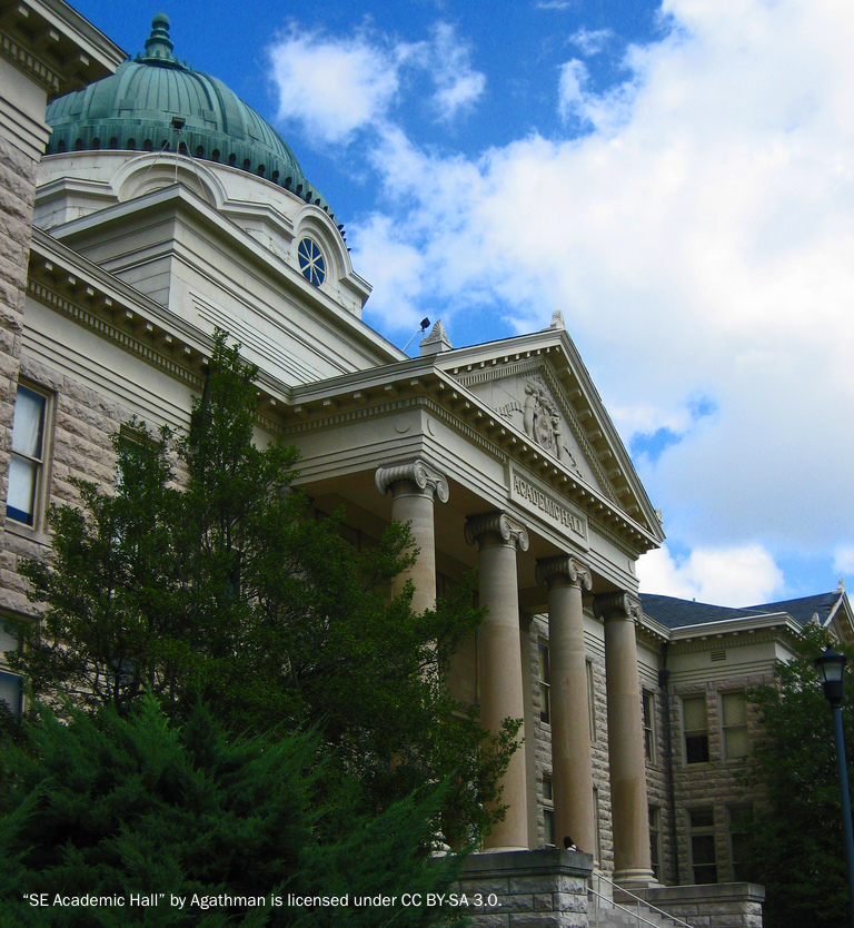 A grand, historic university building of white stone built in classical style with four marble columns at the main entrance and a copper dome.