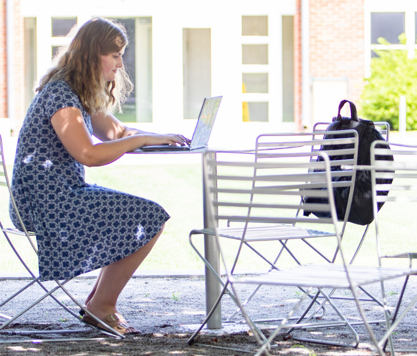 Person sitting at an outdoor table working on a laptop